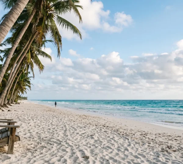 Rangée de cocotiers penchés sur une plage de sable blanc face à une mer turquoise, image emblématique de carte postale tropicale
